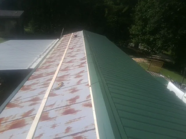 Old rusted panels beside newly installed green metal roofing — Wind Damage Roof Repair by Roofing Brothers in Conklin