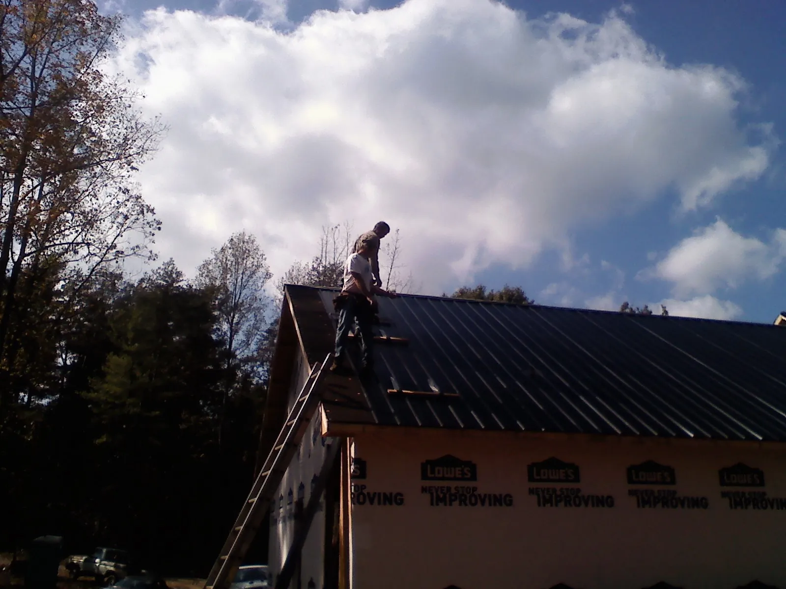Roofer fastening dark metal panels high against a cloudy sky, from a Roof Inspection job in Conklin