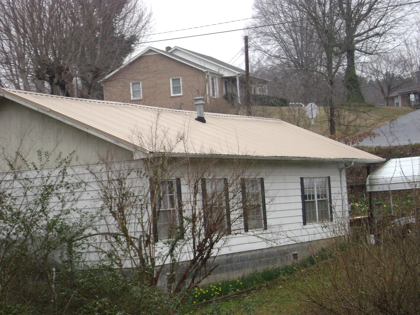 Tan metal roof on a white sided house set into a hillside — Commercial Roofing by Roofing Brothers in Conklin